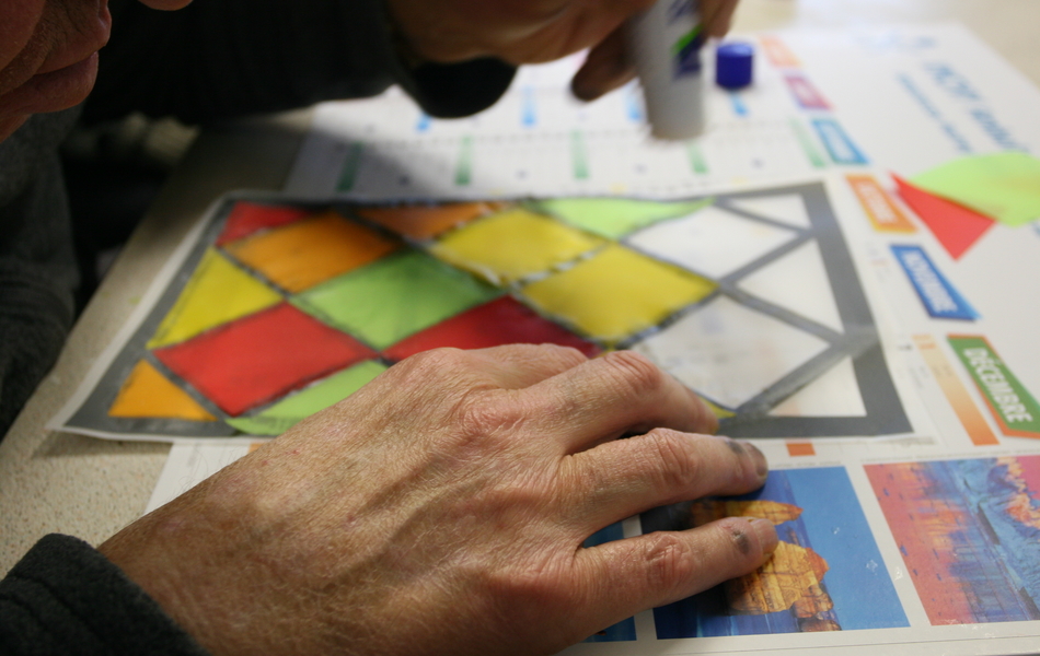 Photo d’un patient réalisant des collages de papiers colorés pour créer un vitrail pendant un atelier.